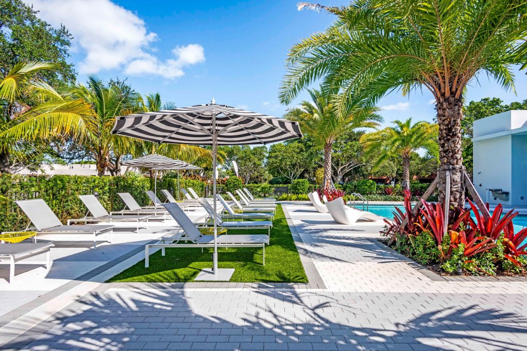 outdoor deck area with shaded seating, swimming pool, and tropical landscaping