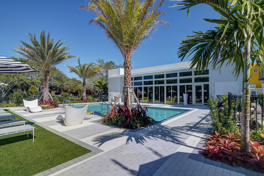 outdoor deck area with shaded seating, swimming pool, and tropical landscaping