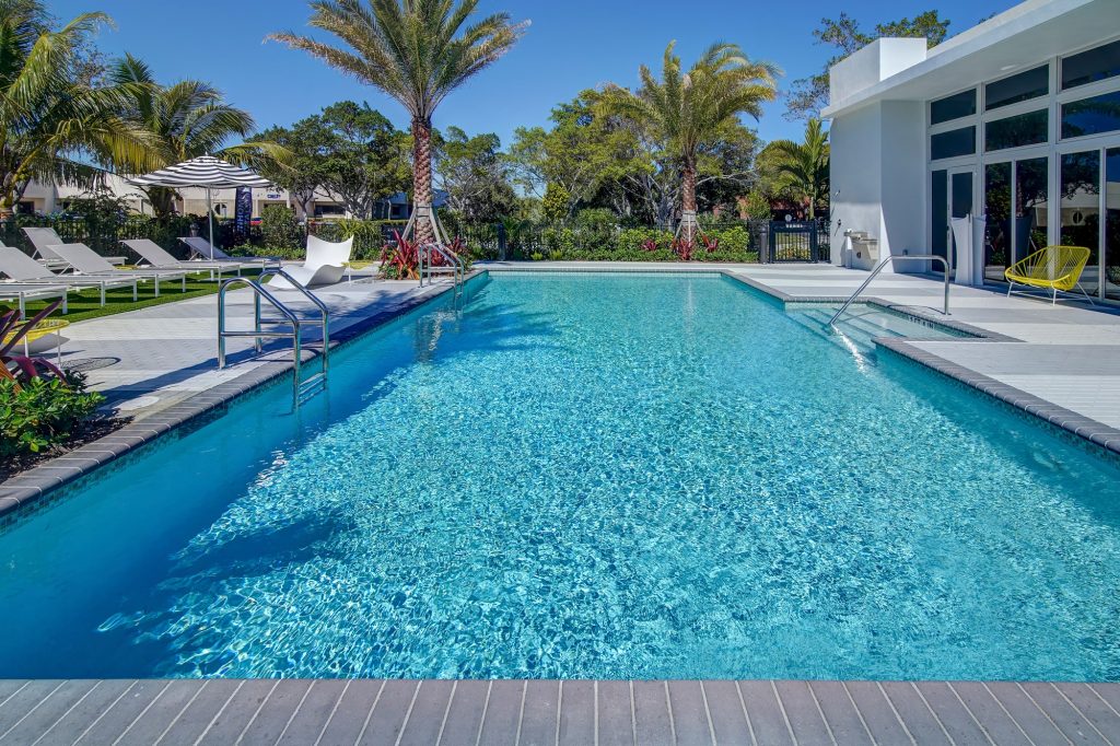 outdoor deck area with shaded seating, swimming pool, and tropical landscaping