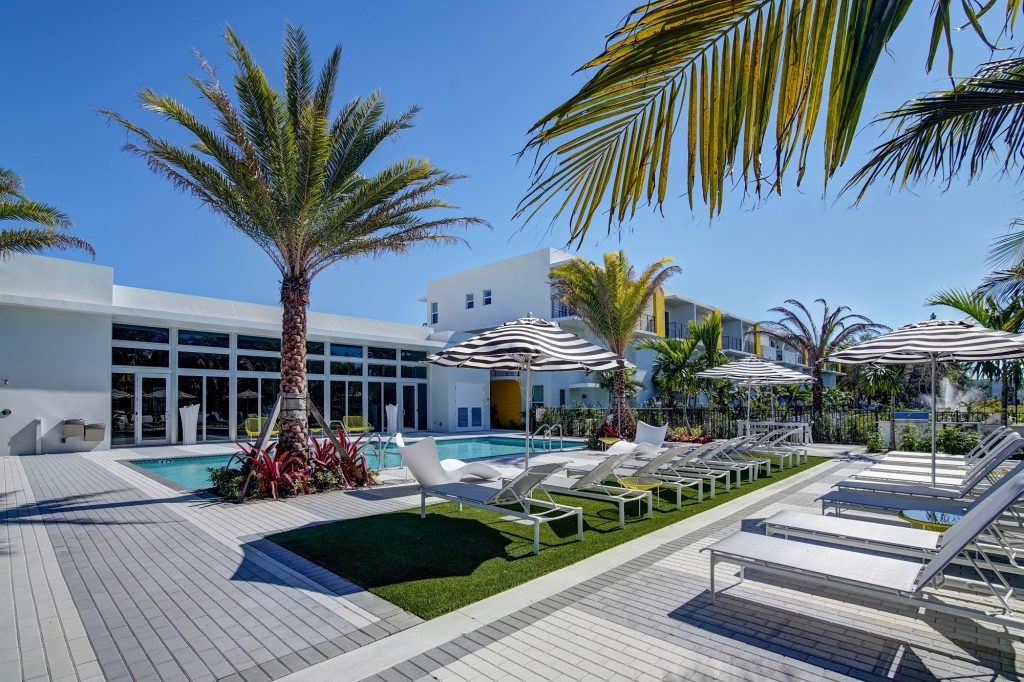 outdoor deck area with shaded seating, swimming pool, and tropical landscaping