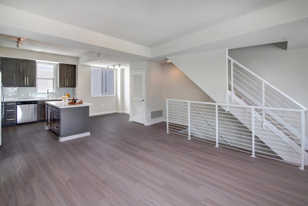 Empty living room area with wood-style flooring and open access to the kitchen