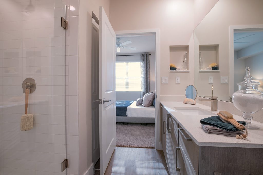 Bathroom area with large mirror, single sink, stand up shower, and wood-style flooring