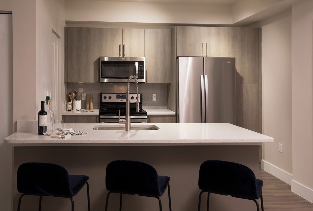 Kitchen area with bar seating, single sink, steel appliances, and wood-style flooring