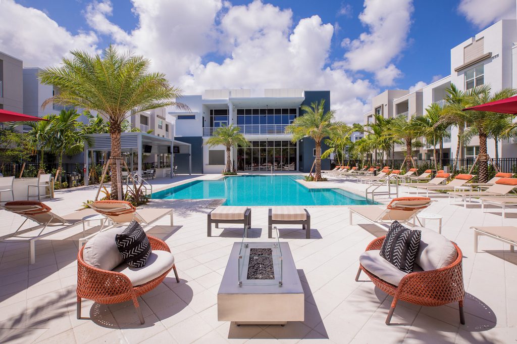 outdoor deck area with shaded seating, swimming pool, and tropical landscaping