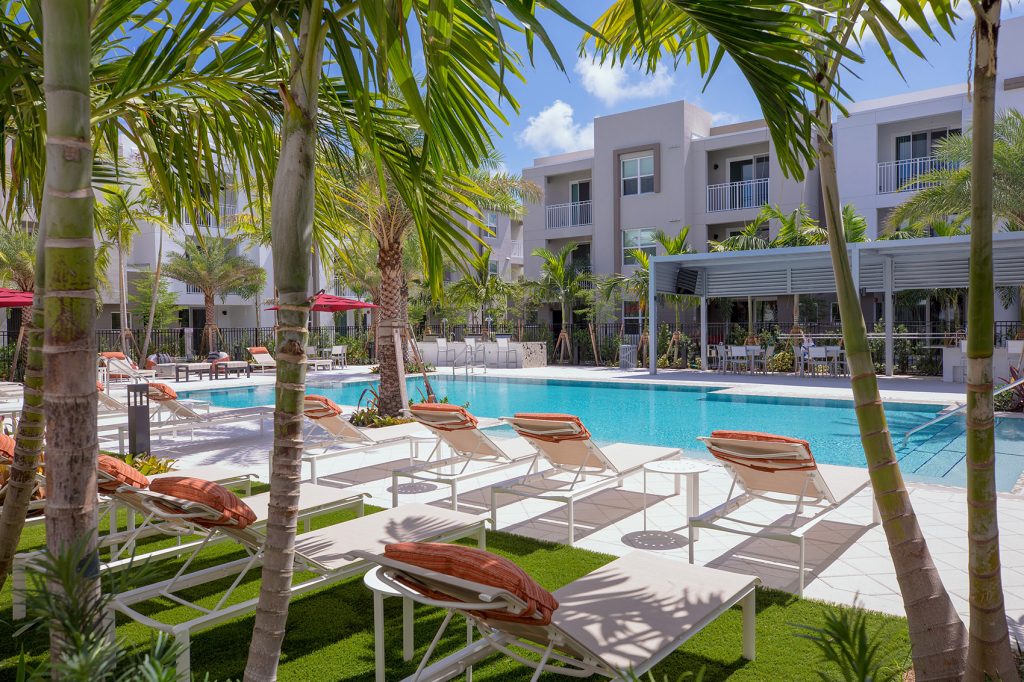 outdoor deck area with shaded seating, swimming pool, and tropical landscaping