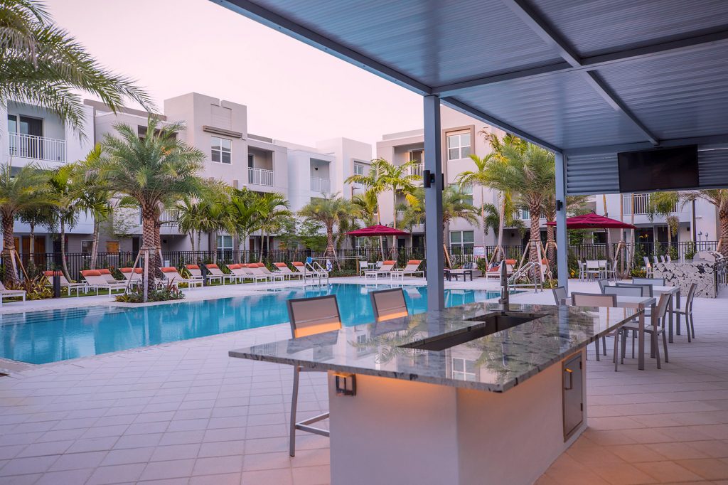 outdoor deck area with shaded seating, swimming pool, and tropical landscaping