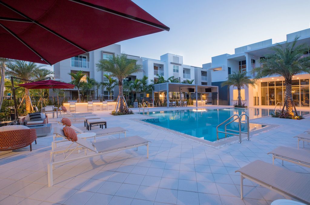 outdoor deck area with shaded seating, swimming pool, and tropical landscaping