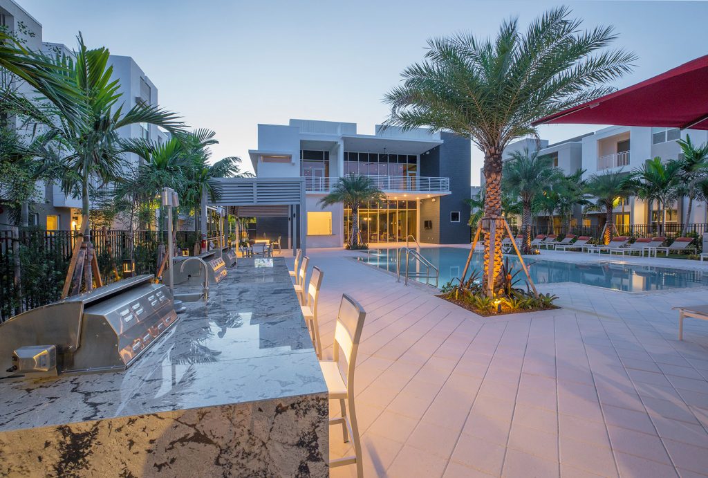 outdoor deck area with shaded seating, swimming pool, and tropical landscaping