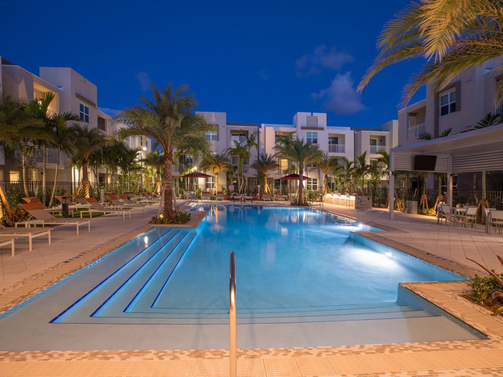 outdoor deck area with shaded seating, swimming pool, and tropical landscaping