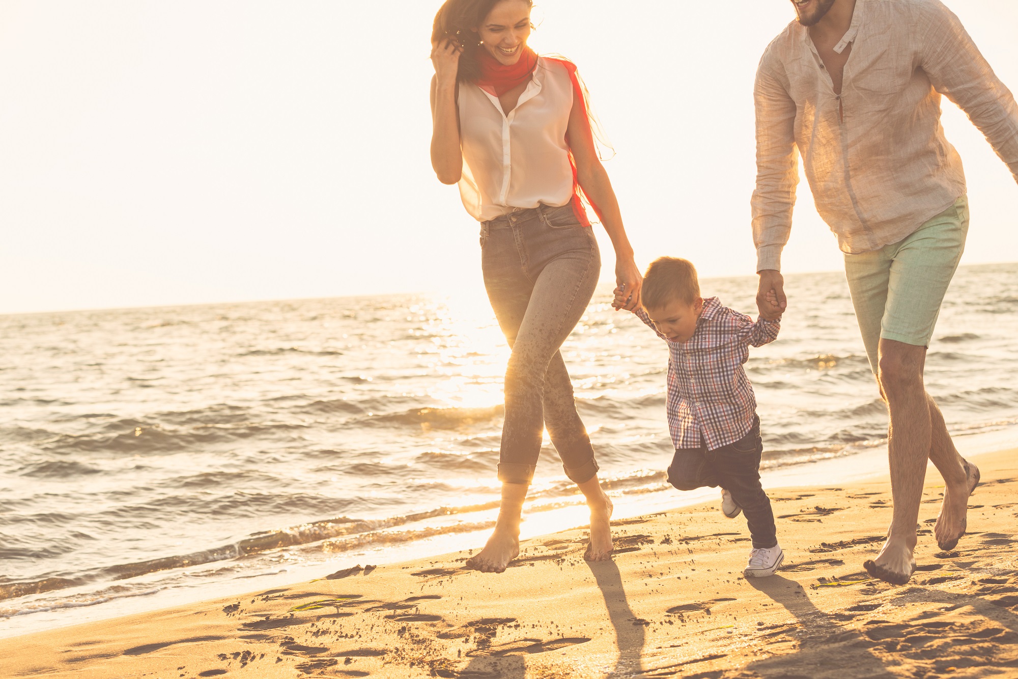 Man and woman holding hands of little boy walking down beach on sunny day