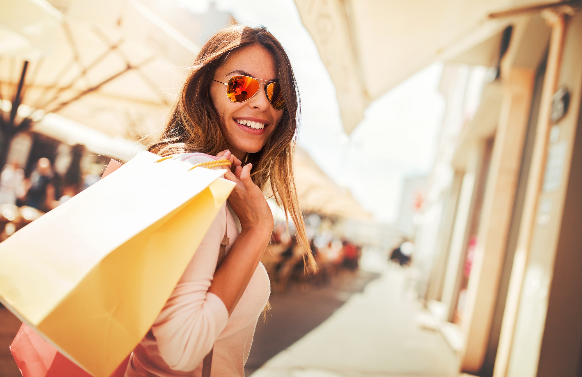 Woman in shades smiling holding shopping bags down mall strip
